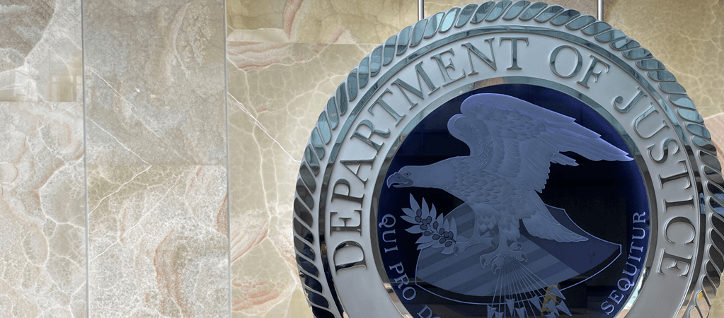 Photo of glass Department of Justice Seal in front of multi-colored wall 