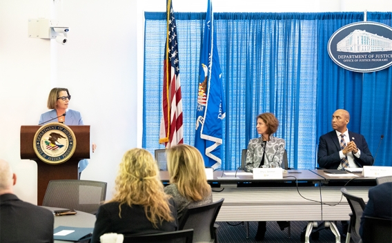 Deputy Attorney General Lisa O. Monaco delivers remarks from a podium at the Office of Justice Programs. She is joined by Assistant Attorney General for the Office of Justice Programs Amy Solomon and Director of the Bureau of Justice Assistance Karhlton F. Moore.