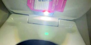 Image of phone taped onto toilet seat in airplane lavatory